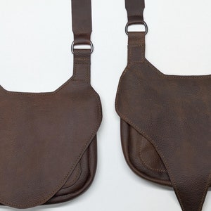 May include: Two brown leather crossbody bags with adjustable straps and metal buckles. The bags have a flap closure and a pointed bottom.