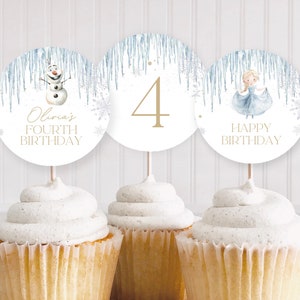 Puede incluir: Tres adornos redondos para cupcakes con temática invernal. Los adornos presentan un muñeco de nieve, el número 4 y una princesa con un vestido azul. El texto en los adornos dice "Olivia's Fourth Birthday" y "Happy Birthday".