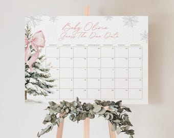 Op de afbeelding: Een babyshowerkalender met de tekst "Baby Olivia Guess The Due Date". De kalender heeft een winterthema met een aquarel illustratie van een besneeuwde kerstboom en een roze strik. De kalender wordt weergegeven op een houten ezel.