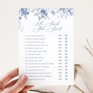 Peut inclure: Une carte blanche avec des motifs floraux bleus en haut. La carte porte le texte "He Said She Said" en écriture cursive. Sous le texte se trouve une liste de 14 affirmations avec des cases à cocher à côté de chaque affirmation. Les cases à cocher sont marquées d'une moustache ou d'une paire de lèvres.