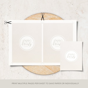 May include: A light beige paper layout with the text "PRINT MULTIPLE PAGES PER SHEET TO SAVE PAPER OR INDIVIDUALLY". The paper has a circular logo that says "Paper Dainty Studio". Scissors are cutting the paper.
