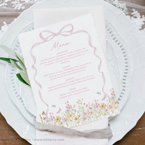 May include: A wedding menu card with a floral design and the word "Menu" at the top. The menu includes appetizers, entrees, dessert, and drinks. The card is on a white plate with a floral design.
