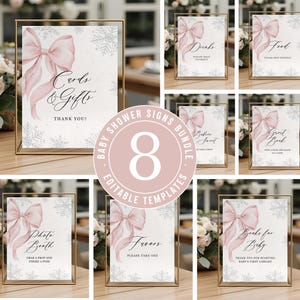 May include: A collection of eight baby shower signs with a gold frame. Each sign features a pink bow and snowflake design. The signs include text for drinks, food, gifts, favors, photo booth, guest book, books for baby, and sweets.