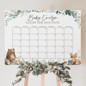 May include: A white baby shower calendar with the text "Baby Evelyn Guess The Due Date". The calendar features a grid for tracking dates, surrounded by watercolor illustrations of woodland animals and greenery. The calendar is displayed on a wooden easel.
