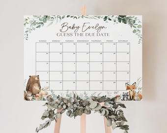 May include: A white baby shower calendar with the text "Baby Evelyn Guess The Due Date". The calendar features a grid for tracking dates, surrounded by watercolour illustrations of woodland animals and greenery. The calendar is displayed on a wooden easel.