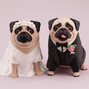 May include: Two pug figurines dressed for a wedding. The left pug wears a white lace dress, a pearl necklace, and a white tiara. The right pug wears a black tuxedo jacket, a white shirt with black buttons, a black bow tie, and a pink rose boutonniere.