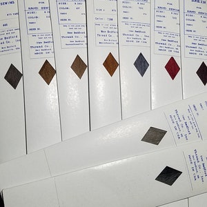 May include: A set of eight spools of waxed thread for hand sewing. The spools are labeled with the brand name "N.B.T. Furrier Waxed Skein" and the color number. The spools are arranged in a row, with the colors ranging from brown to red to gray.