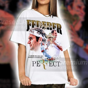 May include: White t-shirt featuring a graphic of Roger Federer with the text "FEDERER" in gold lettering. The shirt includes images of Federer playing tennis and holding a trophy, with the quote "I fear no one but respect everyone."