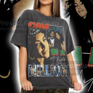 May include: Dark gray t-shirt featuring a graphic of a woman with the text "ONE IN A MILLION" and a group of people. The design includes signatures and the image of a group of people. The shirt has a vintage, worn look.