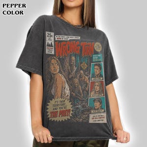 May include: A pepper-colored t-shirt featuring a graphic print styled like a comic book cover for the movie Wrong Turn. The design includes the title, character illustrations, and text such as In the forest, some paths should never be taken.
