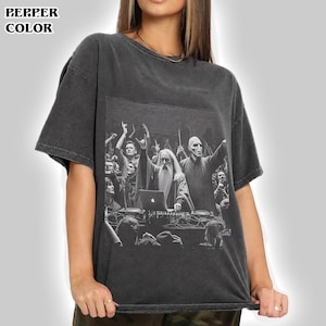 May include: A charcoal gray short-sleeve t-shirt featuring a black and white graphic print of a wizard and a bald figure performing as DJs at a concert. The text PEPPER COLOR is printed in the top left corner of the image in a bold black font.
