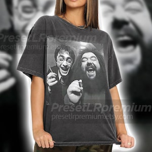 Può includere: T-shirt grigio scuro con un'immagine in bianco e nero di due uomini che ridono. Uno indossa occhiali e tiene in mano un piccolo oggetto, l'altro ha una lunga barba. Il testo "PresetLRpremium presetlrpremium.etsy.com" è visibile.