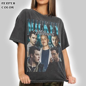 May include: A charcoal grey short-sleeve t-shirt featuring a graphic print of four men. The text "MICKEY" appears in large blue metallic letters above the script word "Milkovich". The shirt has a crew neckline and a vintage-style washed finish.