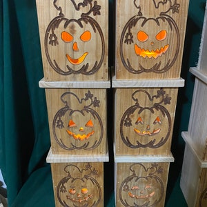 May include: A stack of six wooden boxes with carved pumpkin faces. Each box has a warm, orange glow emanating from the pumpkin face.