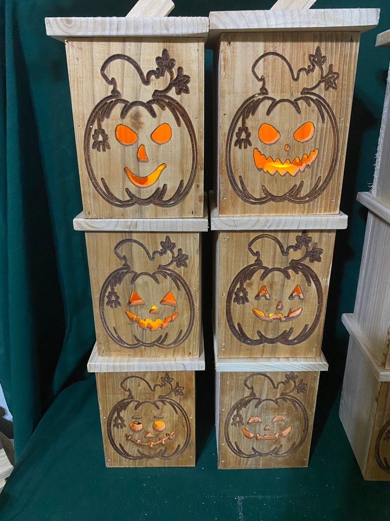 May include: A stack of six wooden boxes with carved pumpkin faces. Each box has a warm, orange glow emanating from the pumpkin face.