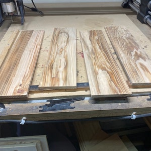 May include: Four pieces of unfinished wood are laid out on a workbench. The wood has a natural grain pattern and is ready for woodworking projects.