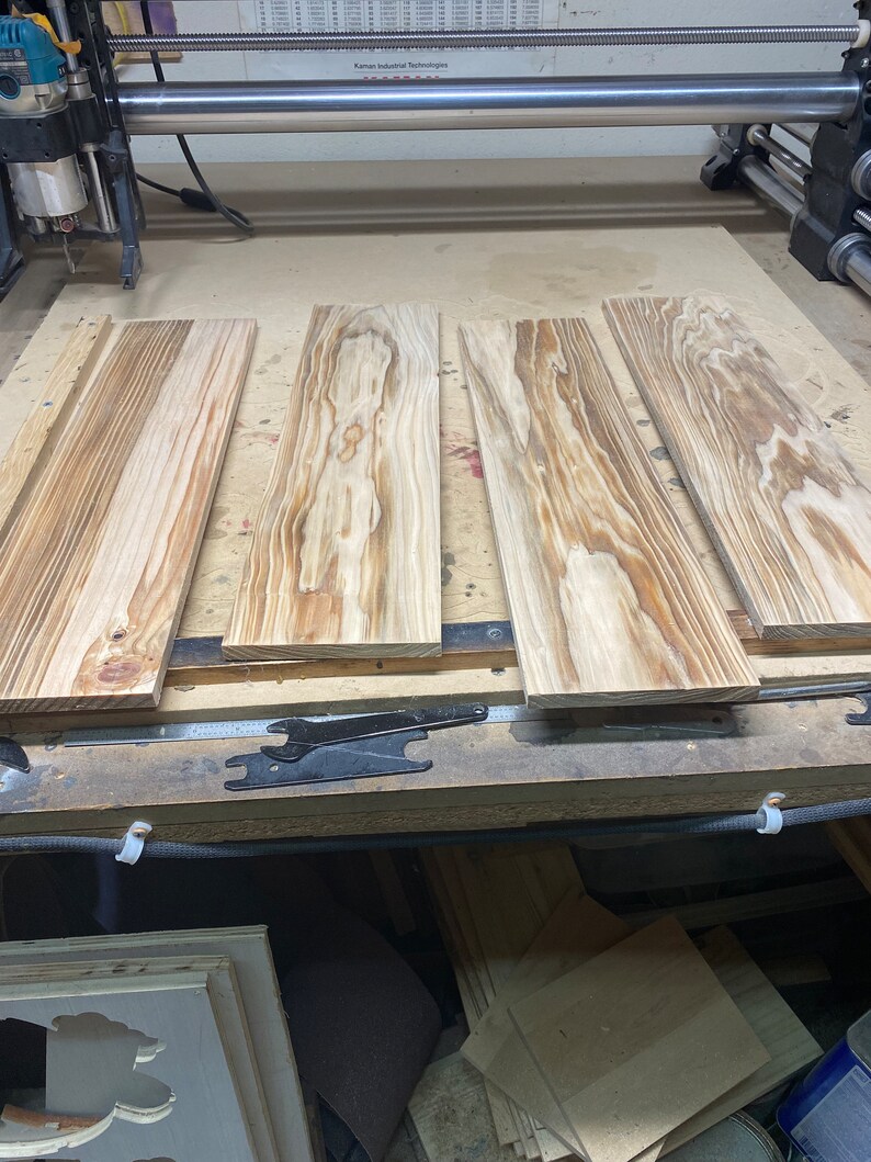 May include: Four pieces of unfinished wood are laid out on a workbench. The wood has a natural grain pattern and is ready for woodworking projects.