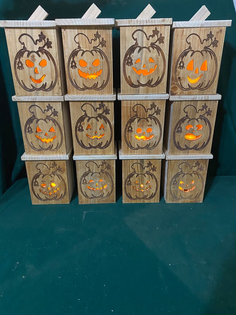 May include: Twelve wooden pumpkin-shaped boxes with carved jack-o'-lantern faces and warm orange lights inside. The boxes are stacked in four rows of three.