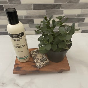 May include: A wooden tray with a small potted succulent plant, a bar of soap, and a bottle of Generic Thickening Liquid. The bottle is white with black text that reads "Generic Value Products Thickening Liquid. Formulated with Paul Mitchell Thicken Up. Adds Body. 8 fl. oz./236 ml."