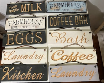 May include: A set of ten wooden signs with gold lettering. The signs have various themes, including farmhouse, coffee, bath, laundry, kitchen, and eggs. The signs are all hung with twine.