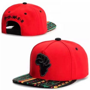 May include: Red baseball cap with a black fist raised in the air over a continent outline on the front. The back of the cap has the word "POWER" embroidered in black. The underside of the brim has a colorful patterned design.