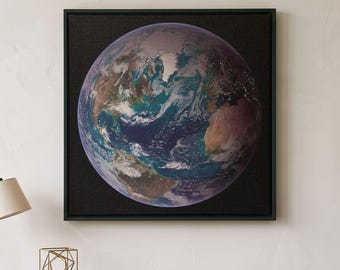 May include: A square wall art piece featuring a detailed circular depiction of Earth against a solid black background, framed in a thin black border. The image shows blue oceans, swirling white clouds, and brown landmasses centered on the wall.