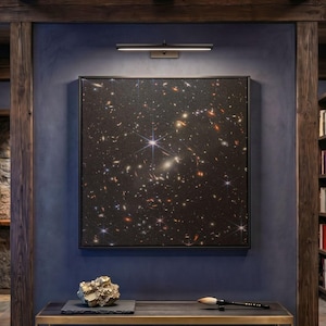 May include: A rectangular metal and wood bench with a lower shelf, featuring a gold-toned frame and a dark surface. On top sits a textured gold-colored rock-like object on a dark slate slab and a long-handled calligraphy brush with a white tip.