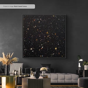 May include: A black framed canvas print of a dark night sky with a scattering of stars and galaxies. The print is hanging on a dark gray wall in a living room setting.