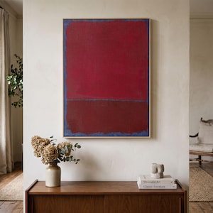 May include: A large rectangular wall art piece featuring two stacked blocks of deep red and dark maroon color, framed in a light wood border. The painting displays a textured surface with a thin blue outline visible along the edges of the color fields.