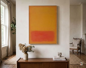 Könnte beinhalten: Ein rechteckiges Wandkunstwerk bestehend aus einer großen vertikalen Leinwand mit einem strukturierten goldgelben oberen Bereich und einem einfarbigen orangeroten unteren Bereich, gerahmt in einem hellen Holzrahmen, an einer weißen Wand.