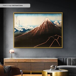 Op de afbeelding: Een goudomrand canvas print van een traditioneel Japans landschap met de berg Fuji. Het kunstwerk toont de berg met een besneeuwde top tegen een blauwe lucht met witte wolken. De print heeft Japanse tekst in de linkerbovenhoek.