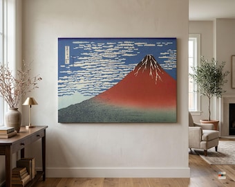 Può includere: Una stampa artistica da parete rettangolare che raffigura una montagna rossa con una cima scura su un cielo blu pieno di nuvole bianche orizzontali. L'opera include un testo giapponese verticale nell'angolo in alto a sinistra della stampa.