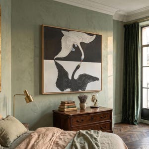 Puede incluir: Una gran obra de arte mural rectangular enmarcada que presenta un cisne blanco sobre un fondo negro encima de un cisne negro sobre un fondo blanco, con las dos aves tocándose los picos en el centro. La obra está en un marco de madera clara.