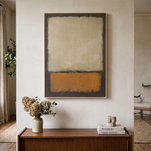 Op de afbeelding: Een rechthoekig wandkunstwerk met een groot, lichtbeige centraal blok omrand door een donker houtskoolkleurig kader, met een effen horizontale band van dieporanje aan de onderkant, gevat in een dunne, lichtgekleurde houten lijst.