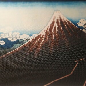 Op de afbeelding: Close-up van een stof met een landschap in Japanse stijl. De afbeelding toont een berg met een besneeuwde top, tegen een blauwe lucht met witte wolken. De berg is bruin met witte accenten. De stof heeft een getextureerde uitstraling.