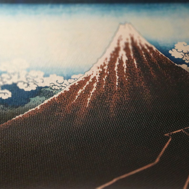 Op de afbeelding: Close-up van een stof met een landschap in Japanse stijl. De afbeelding toont een berg met een besneeuwde top, tegen een blauwe lucht met witte wolken. De berg is bruin met witte accenten. De stof heeft een getextureerde uitstraling.