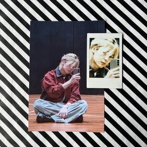 Può includere: Un collage con una persona che scatta un selfie con uno smartphone. La persona indossa una giacca rossa e pantaloni grigi, seduta su un pavimento di legno. Una foto più piccola in stile Polaroid mostra un primo piano del selfie. Lo sfondo presenta un motivo a strisce bianche e nere.