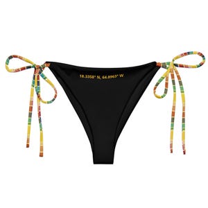 Op de afbeelding: Zwarte bikinibroek met kleurrijke gestreepte bandjes in geel, rood, groen en bruin. De tekst "18.3358° N, 64.8963° W" is in goud op de voorkant gedrukt. Een stijlvol badkledingartikel.