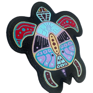 Peut inclure: Un patch en tissu noir avec un motif de tortue brodé coloré. La tortue est soulignée de fil doré et a une carapace violette, bleue et rouge avec des accents noirs et blancs.