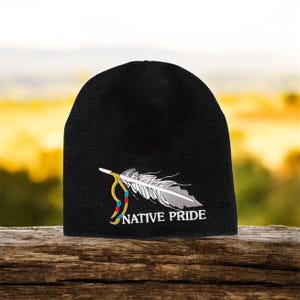 May include: Black beanie hat with a Native Pride design. The design features a white and grey feather with yellow and red accents, and the words "NATIVE PRIDE" in white.