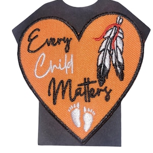 May include: Orange heart-shaped patch with the text "Every Child Matters" in black lettering. A white feather with a red tip is on the right side of the heart. Two white footprints are at the bottom of the heart.