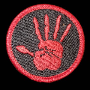 Op de afbeelding: Rode geborduurde handafdruk patch op een zwarte achtergrond met een rode gestikte rand.