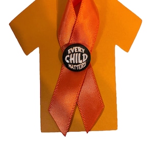 May include: Orange ribbon tied in a bow on a yellow paper cutout of a t-shirt. The ribbon has a black button with the text "Every Child Matters" in white.