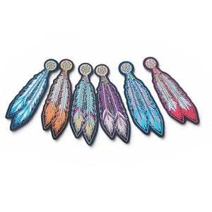 May include: A collection of embroidered feather patches in shades of blue, orange, teal, purple, and red. Each patch has a dreamcatcher design at the top. The feathers are intricately stitched.