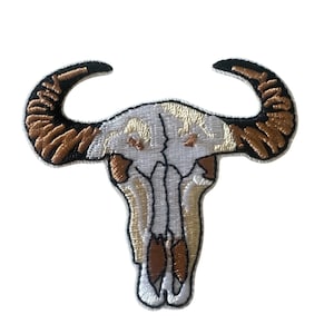 May include: Embroidered patch of a white buffalo skull with brown horns. The skull has a detailed design with intricate lines and shading.