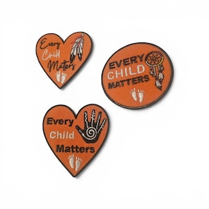 May include: Three orange embroidered patches with black borders. Two are heart-shaped and one is circular. All feature the text "Every Child Matters" in black or white, accompanied by imagery of feathers, a dreamcatcher, a handprint, and footprints.