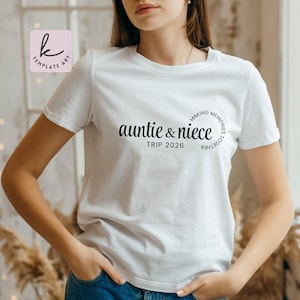 以下が含まれることがあります： 黒い文字で「auntie & niece TRIP 2026」と書かれた白いTシャツ。「MAKING MEMORIES TOGETHER」の文字が「auntie & niece」の周りに円を描いています。