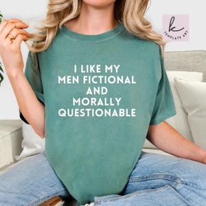 May include: A teal t-shirt featuring the white text: "I LIKE MY MEN FICTIONAL AND MORALLY QUESTIONABLE". The shirt is a relaxed fit, suitable for casual wear.