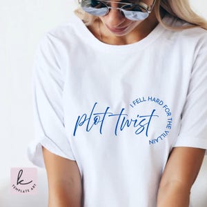 Op de afbeelding: Wit T-shirt met de blauwe tekst "plot twist" in een cursief lettertype. De tekst is omcirkeld door de zin "I fell hard for the villain". Het T-shirt heeft een casual stijl.