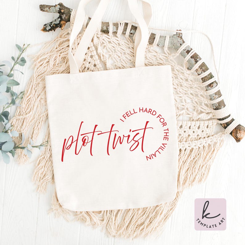 Op de afbeelding: Een witte canvas draagtas met rode tekst die "plot twist" leest in een cursief lettertype, met de zin "I fell hard for the villain" in een cirkelvormig lettertype eromheen. De tas heeft twee handvatten en wordt op een neutrale achtergrond gepresenteerd.
